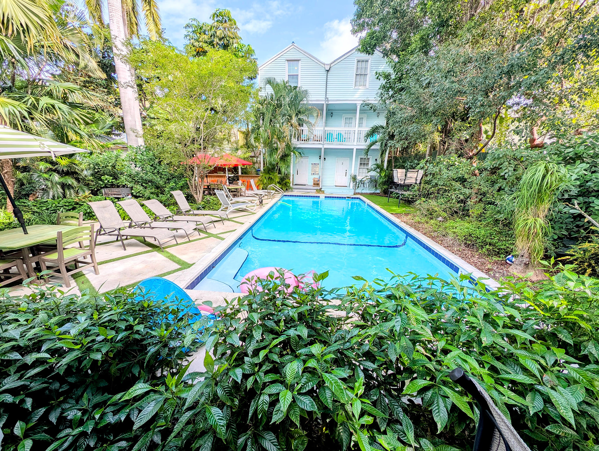 Tropical pool oasis with loungers, dining area, and balcony views.