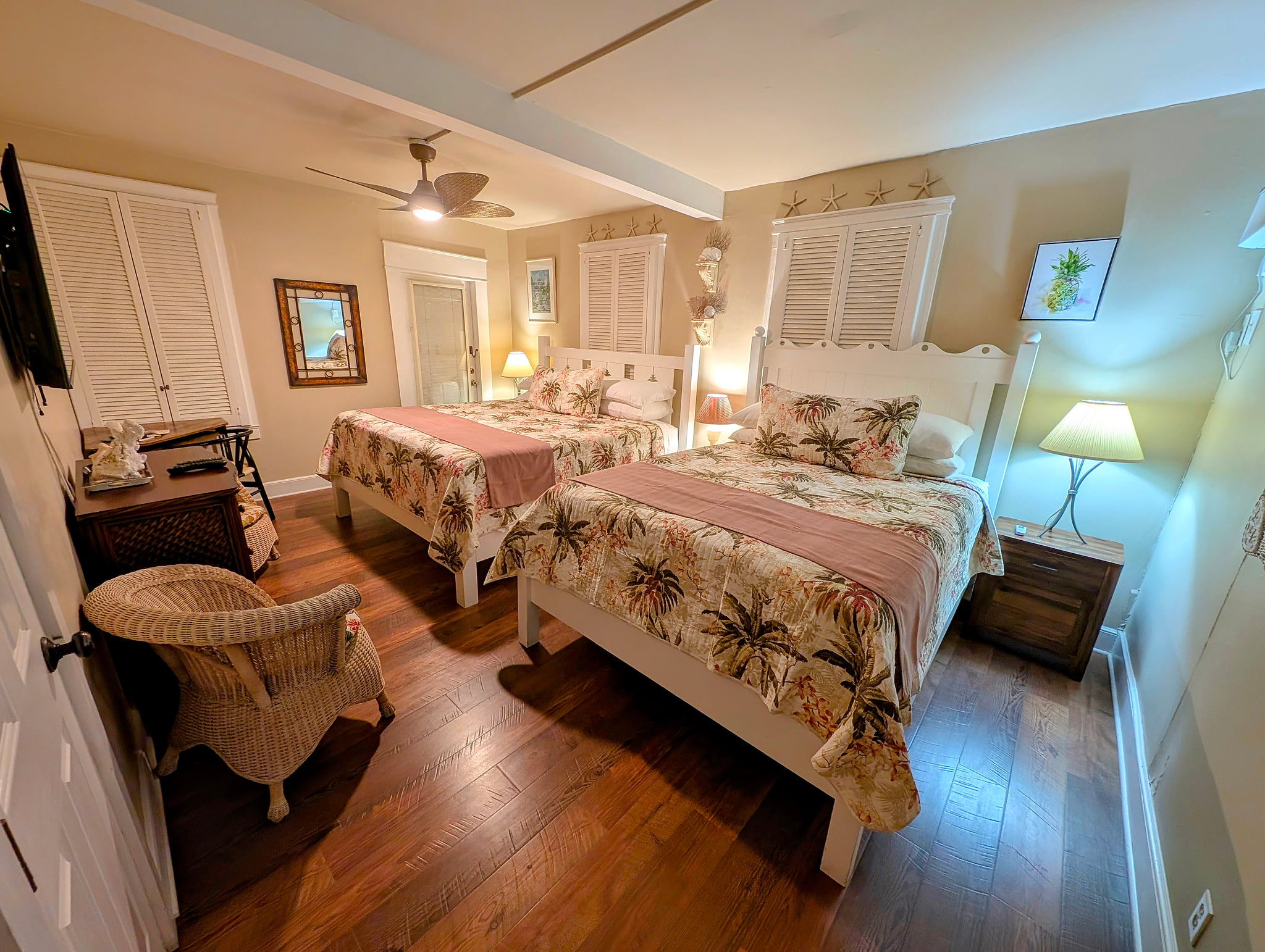 Coastal retreat: two comfy beds, hardwood floors, fan, and warm lighting.