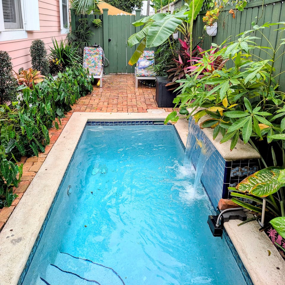 Private tropical plunge pool with waterfall and sunny brick patio