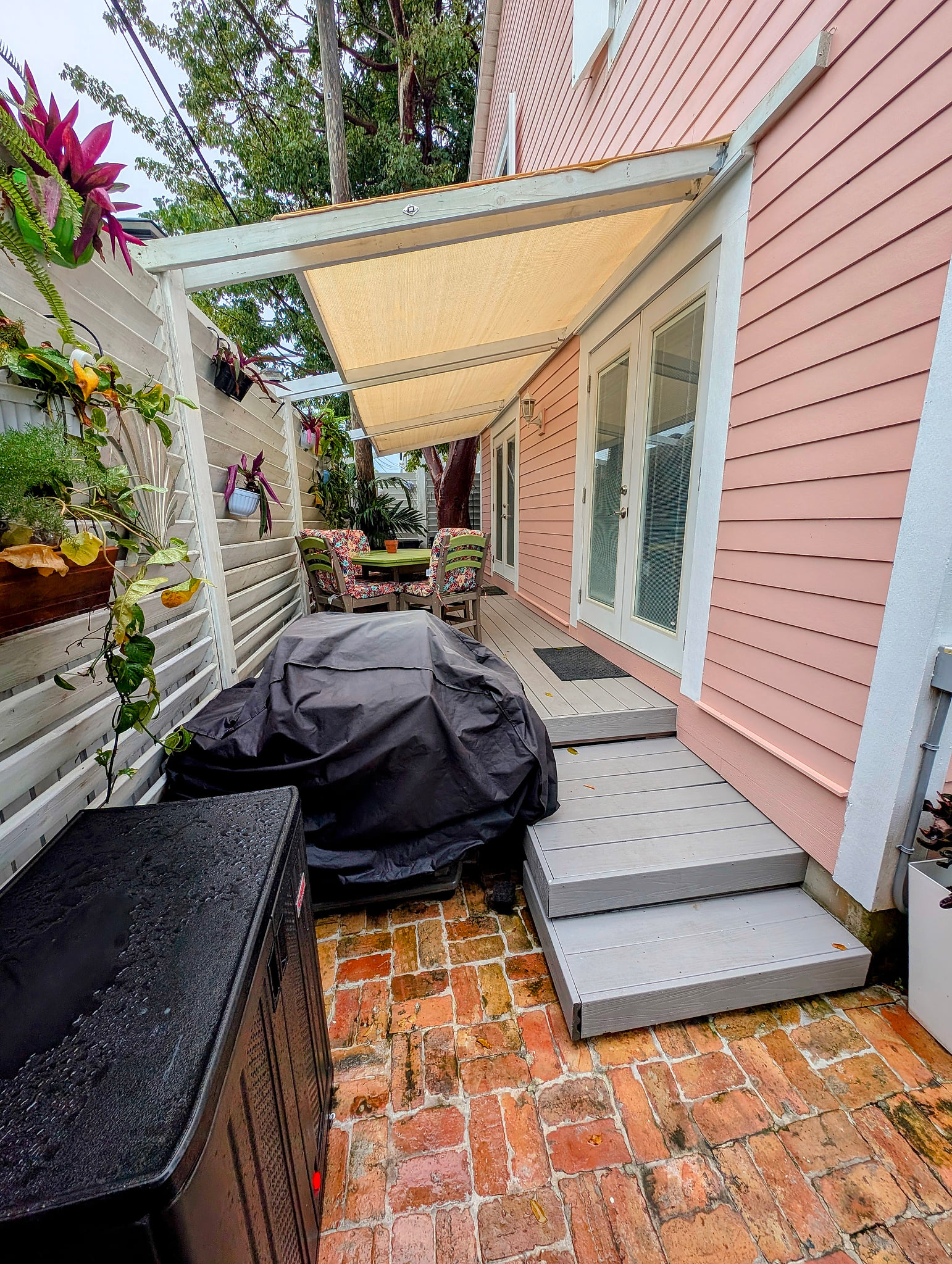 Shaded patio with grill, dining set, and tropical vibes by French doors.