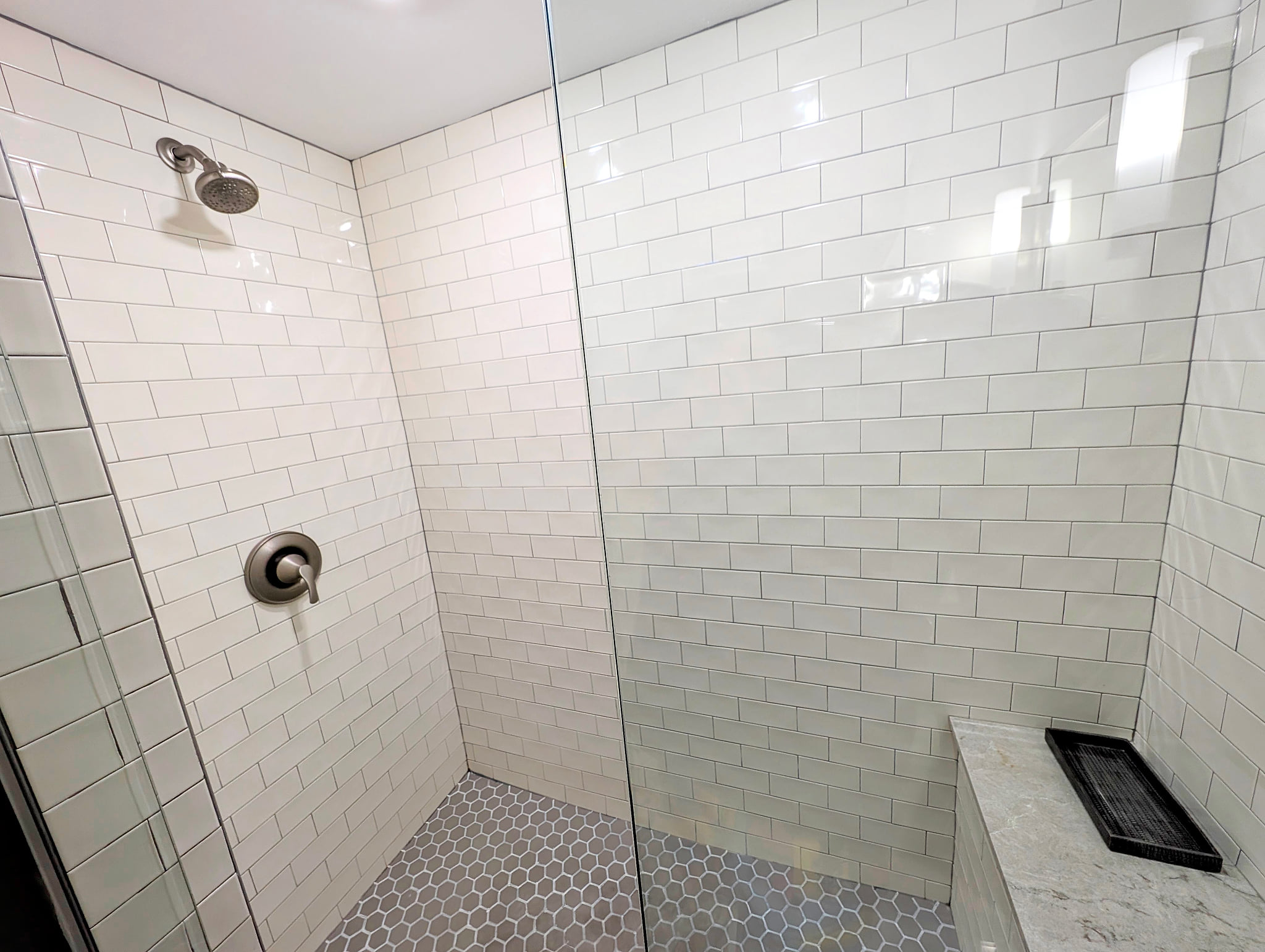 Spacious walk-in shower with subway tile, hex floor, and bench seating