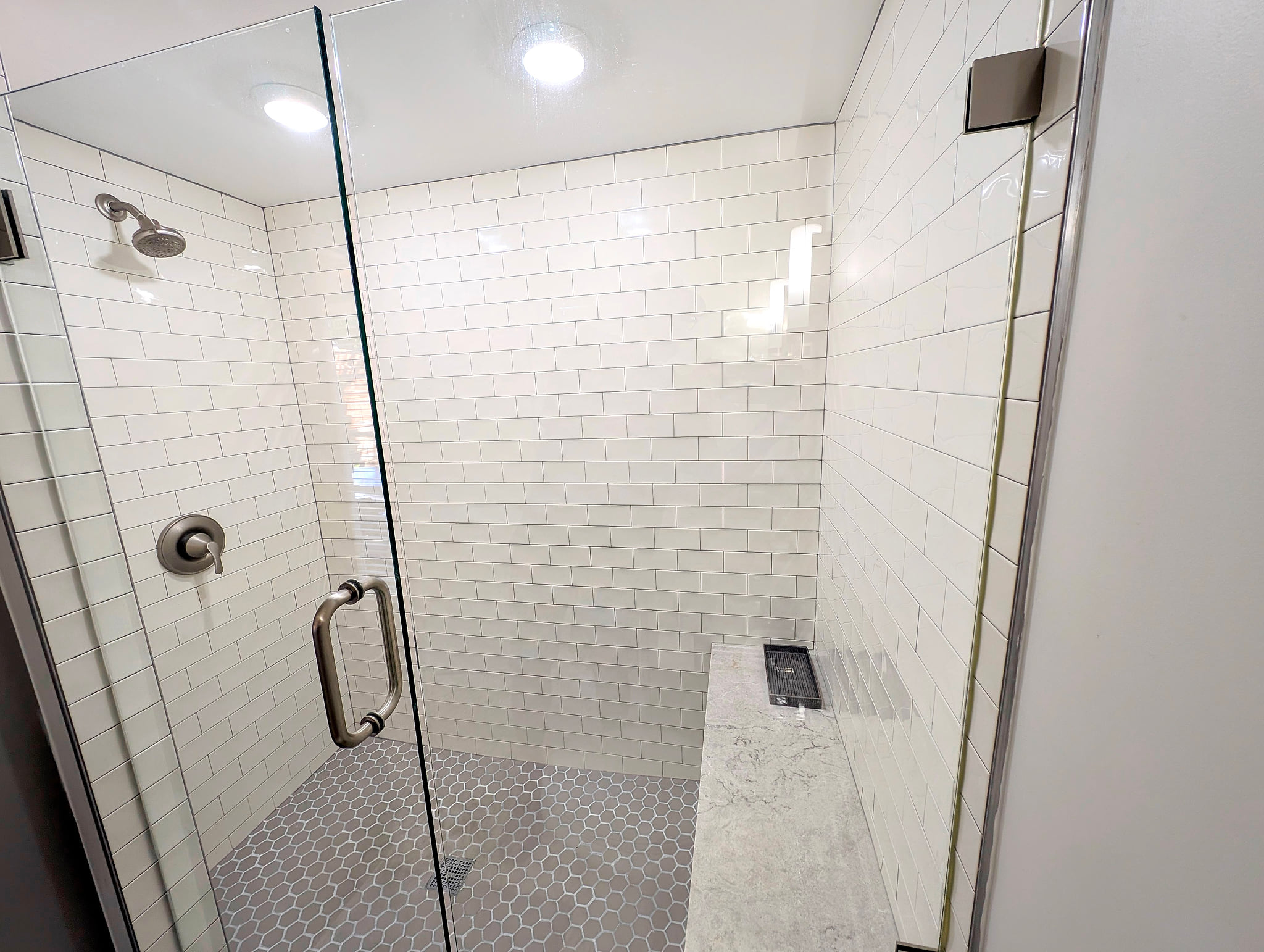 Spacious walk-in shower with bench, subway tile, and glass enclosure.