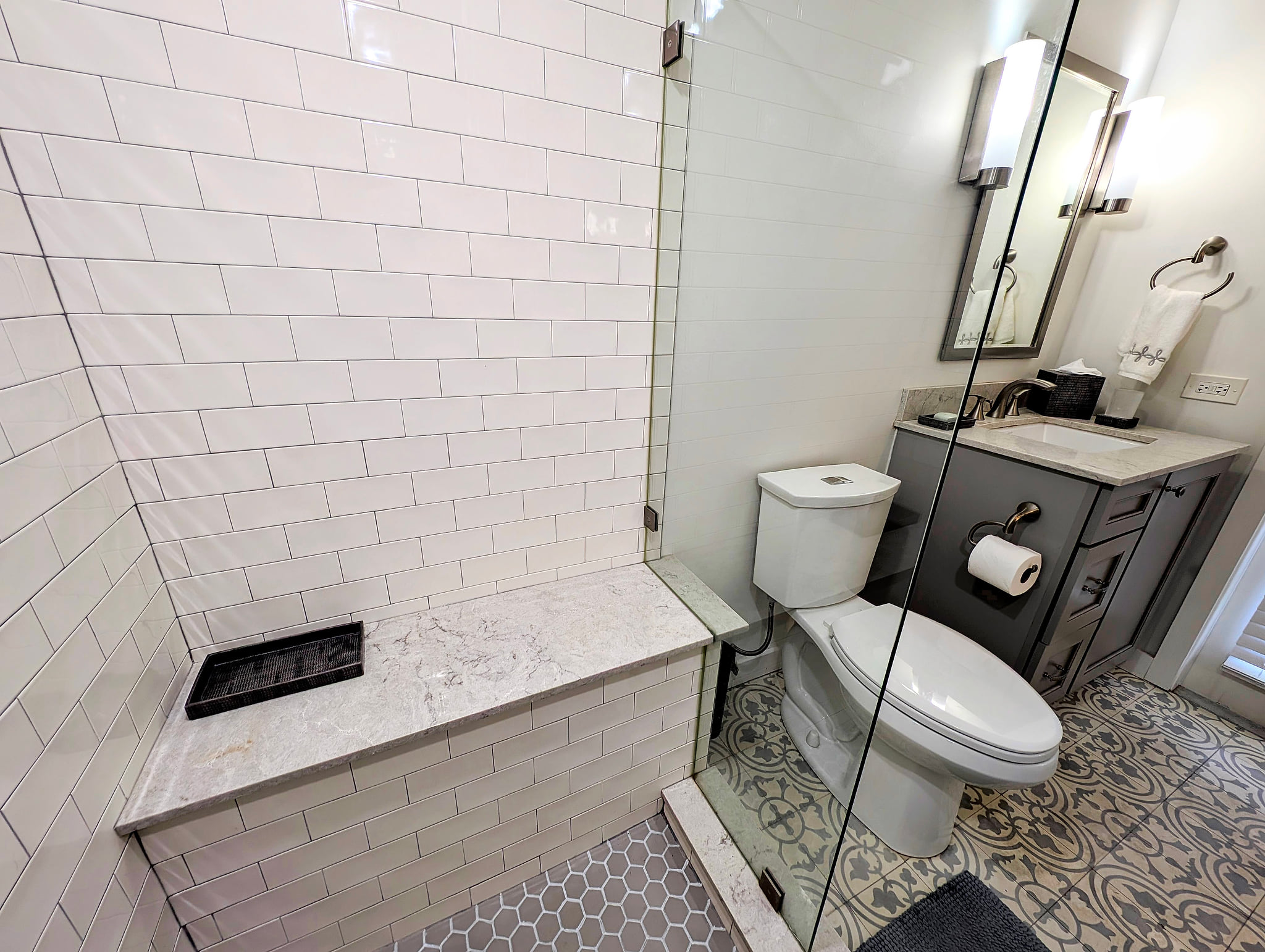 Modern bath: glass walk-in shower, quartz bench, chic patterned floor.