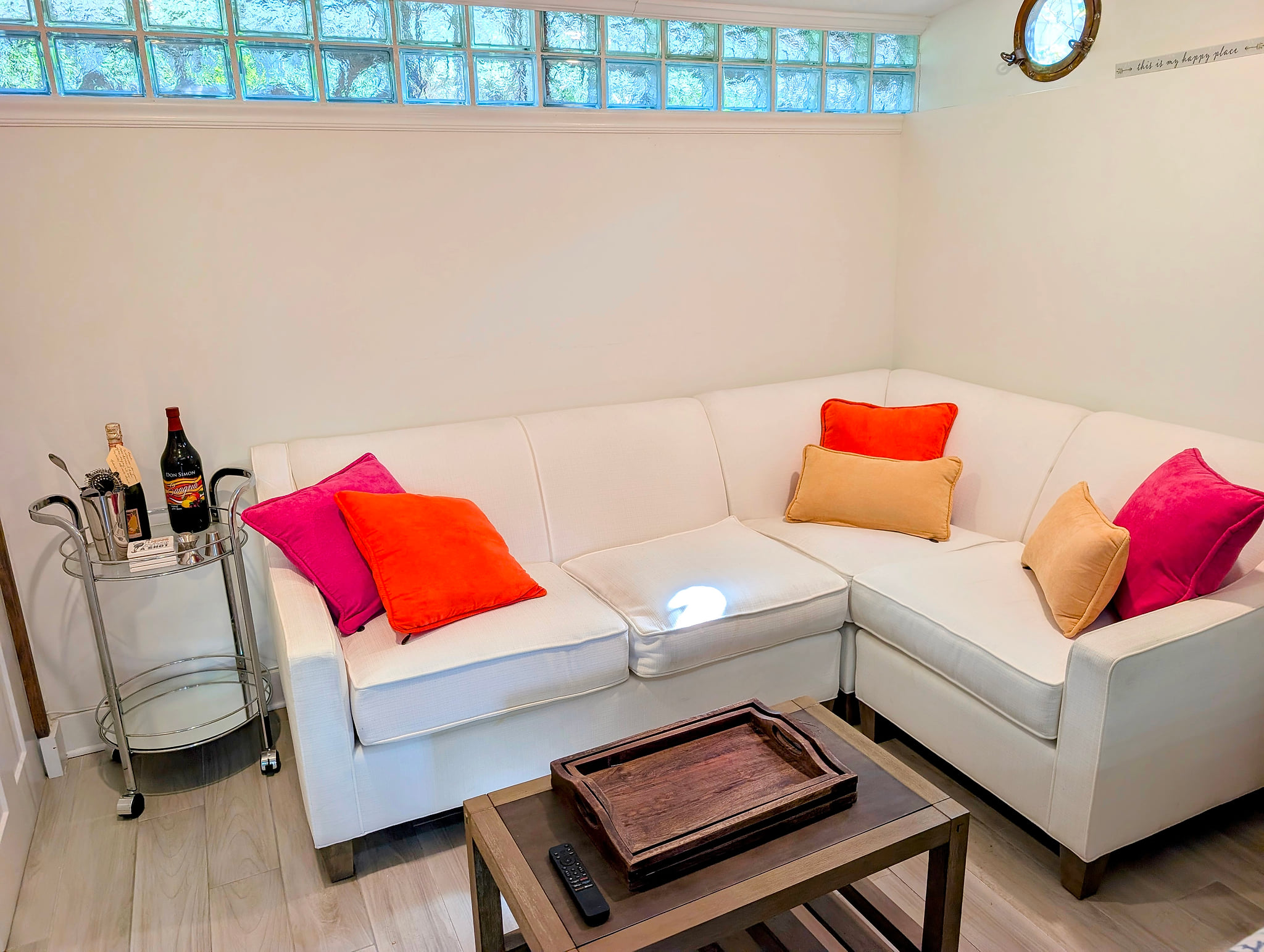 Sunny lounge with white sectional, bar cart, and glass-block window glow