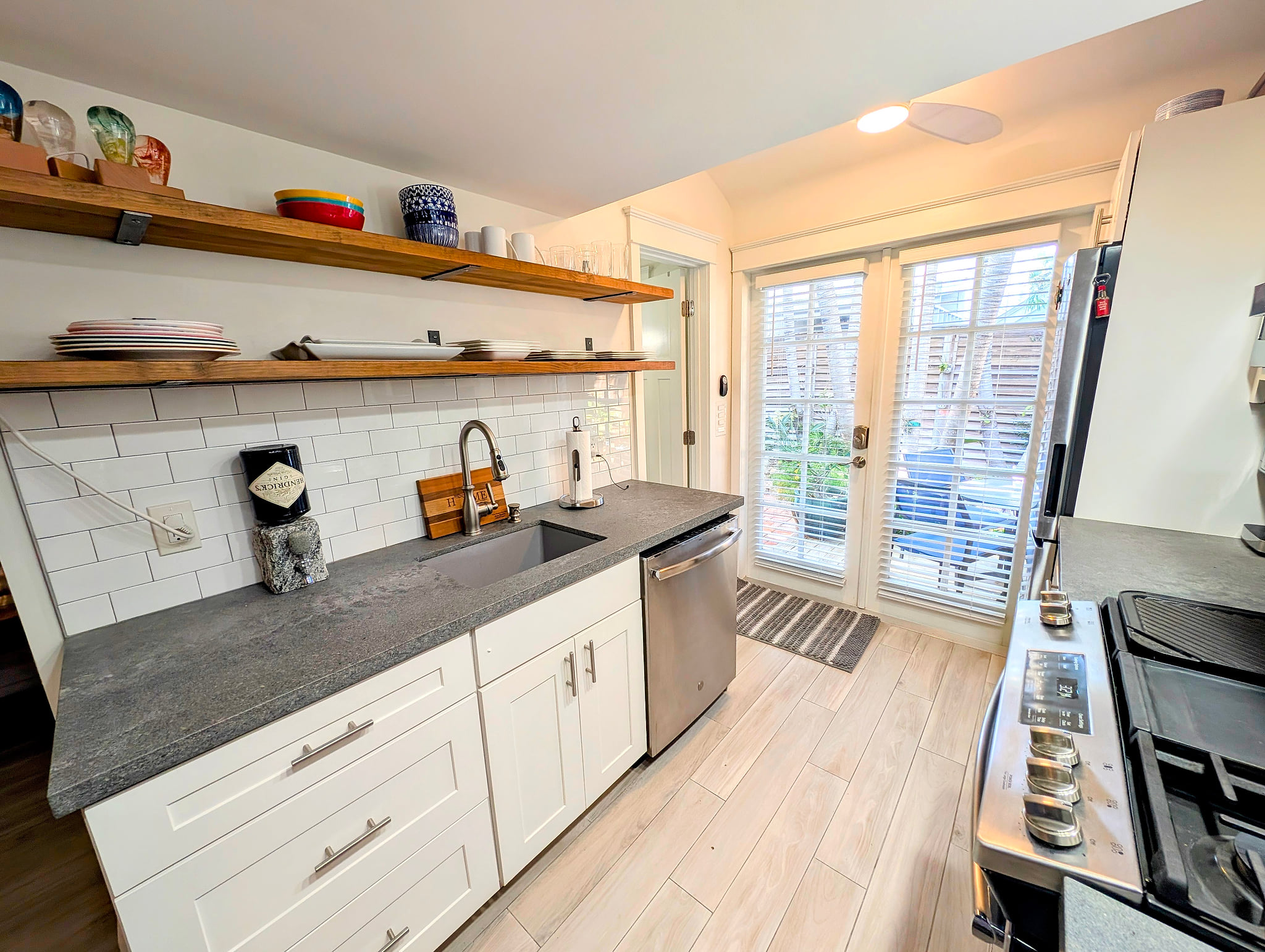 Bright galley kitchen with quartz, open shelves & patio doors, stainless appliances