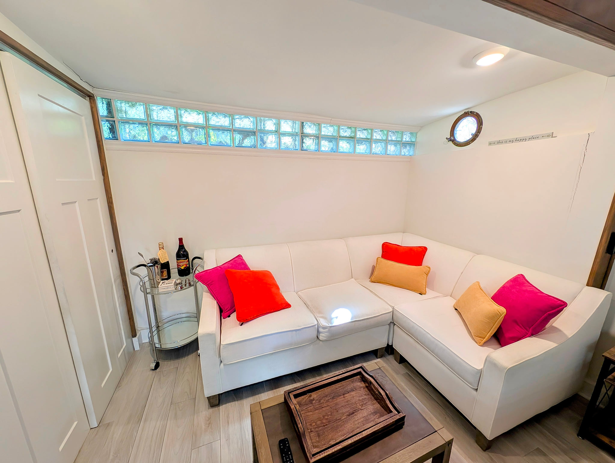 Cozy lounge with white sectional, bar cart, and sunlit glass-block windows