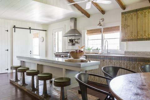 Sunny farmhouse kitchen with long island, exposed beams & vintage stools