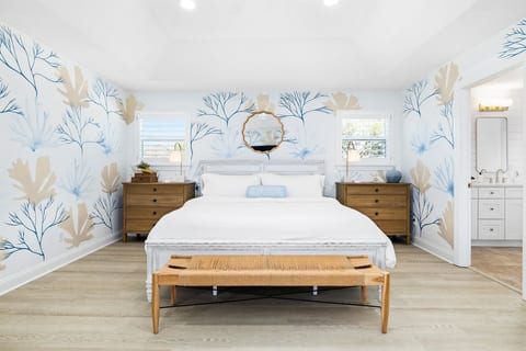 Serene primary suite with a king bed, coastal mural accents, and plenty of natural light — designed for restful nights after a day at the beach