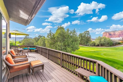 Expansive private deck with cozy wicker seating and vibrant orange cushions. Enjoy breathtaking views of the lush golf course and Sedona's iconic red rocks under a beautiful blue sky. Perfect for relaxation.