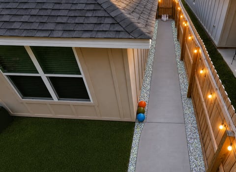 Lit side yard walkway with privacy fence, turf, and fun game area