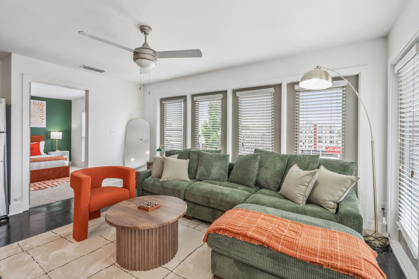 Sunlit living room with sectional, accent chair, and views into the bedroom.