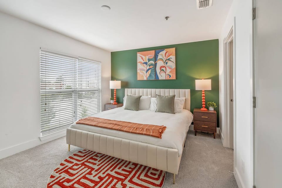 Peaceful bedroom with green accent wall, tufted headboard, and large picture window.