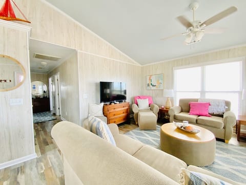 This open-concept floor plan with ceiling fans, large windows with blinds, and a sky-blue ceiling induces calm.