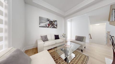 Relax in this stylish, sunlit lounge featuring comfortable sofas, a glass coffee table, elegant art décor, and a cozy area rug.