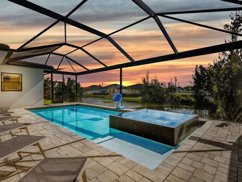 Unwind poolside at sunset in the screened lanai, featuring a private pool, spa, lounge seating, and waterfront views.