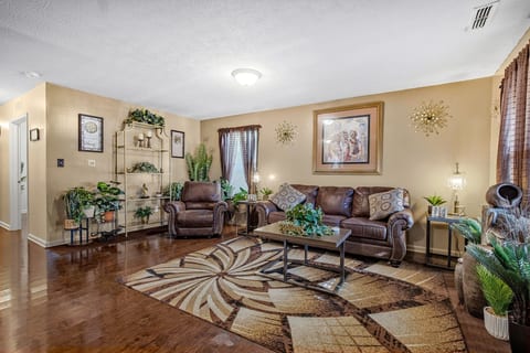 Cozy living room with leather seating, hardwood floors, and lush greenery.