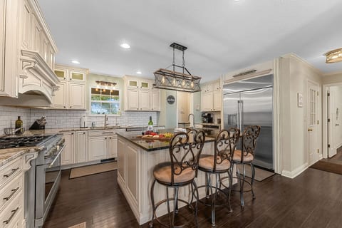 A pro-grade 6-burner range, herringbone subway tile backsplash, a granite island with seating for four, and a wine fridge stocked and ready. This kitchen was built for real cooking.