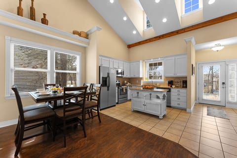 Open dining table and kitchen under a vaulted ceiling with skylights. Plenty of room to gather, with the deck door close by.