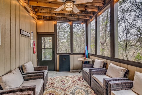 Screened porch with wicker lounge chairs and cornhole. String lights and a ceiling fan make it an easy spot for a game and a cold drink.