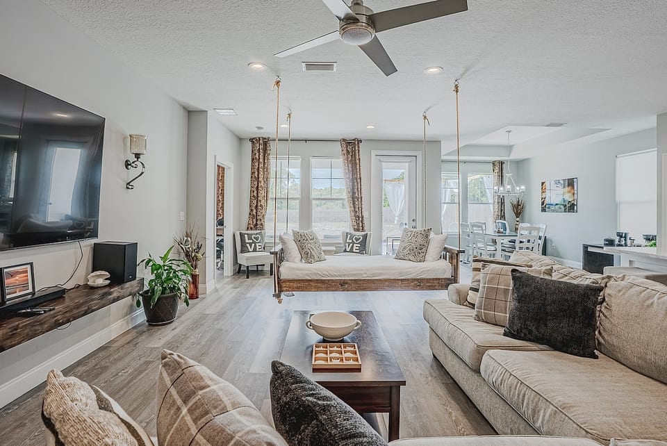 Relax in style! This bright living area features a unique indoor hanging daybed, cozy sectional, and a large smart TV. Modern meets comfort with rustic accents, perfect for movie nights or afternoon naps in a sun-drenched, open-concept space.