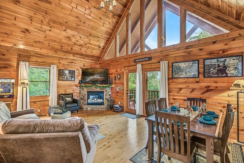 Cozy log cabin great room with stone fireplace, deck access, and tall windows
