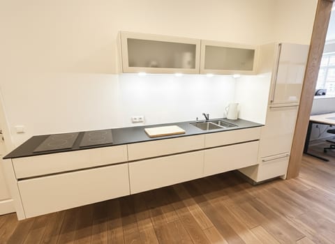 Sleek kitchenette with induction hobs, double sink & under-cabinet lighting