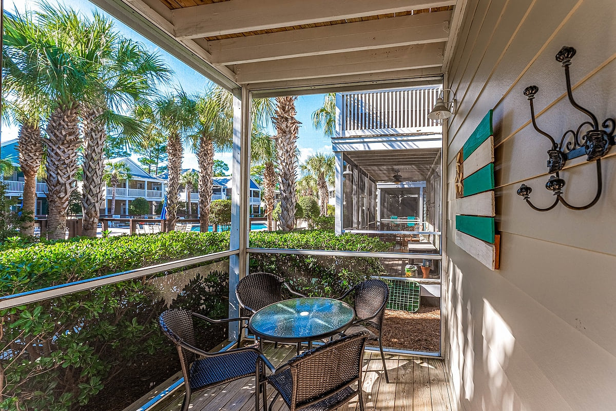 Screened porch with glass-top table and wicker chairs. Surrounded by palm trees and garden views, it’s a bright, relaxing outdoor space perfect for gathering or unwinding.