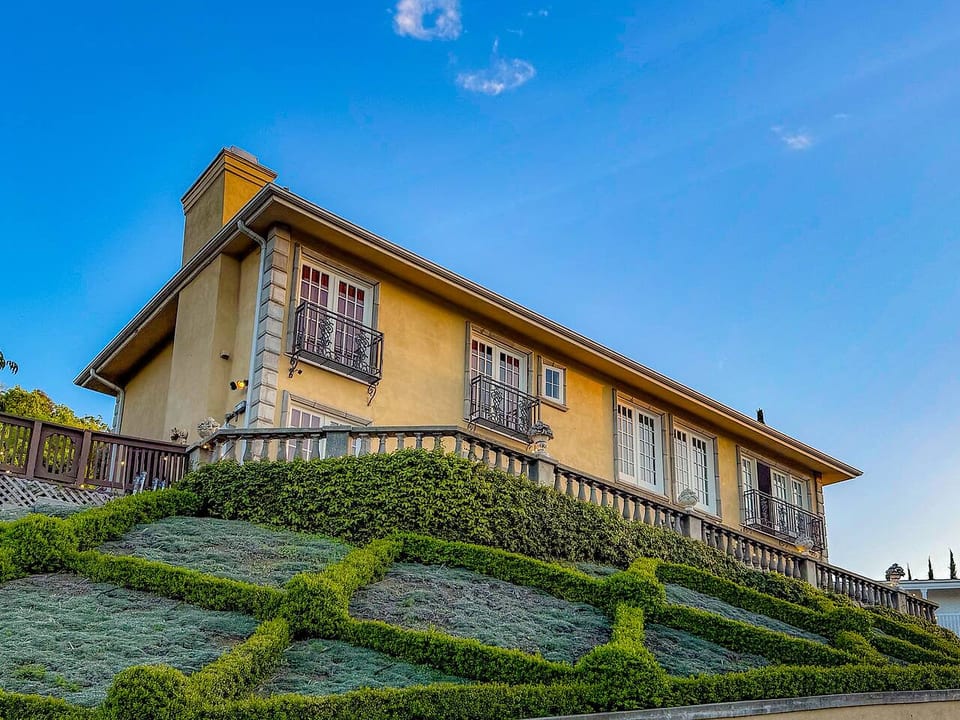 Elegant front exterior of a luxury Spanish-style villa, featuring manicured geometric landscaping, classic stucco walls, and wrought-iron balcony details. This elevated façade blends timeless architecture with stunning curb appeal and panoramic views