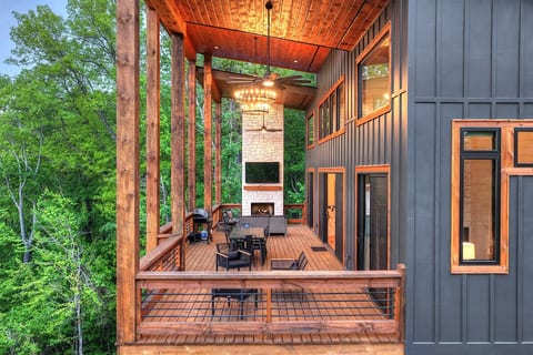 Covered upper deck with outdoor fireplace, chandelier, and treetop dining among the forest. Outdoor TV