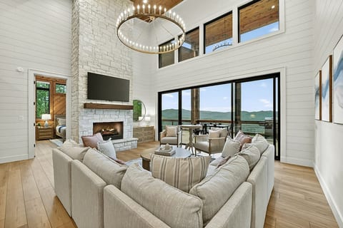 Soaring two-story living room with stone fireplace, grand chandelier, and panoramic mountain views