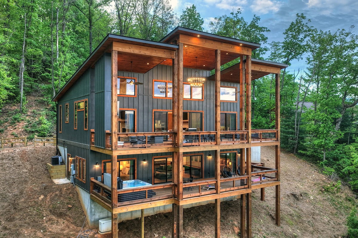 Two-level cabin with wraparound decks, warm wood accents, and hot tub nestled in the woods