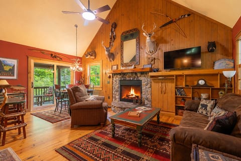 The spacious living room features vaulted ceilings, comfortable seating, a smart TV, and a cozy wood-burning fireplace at the heart of the cabin.