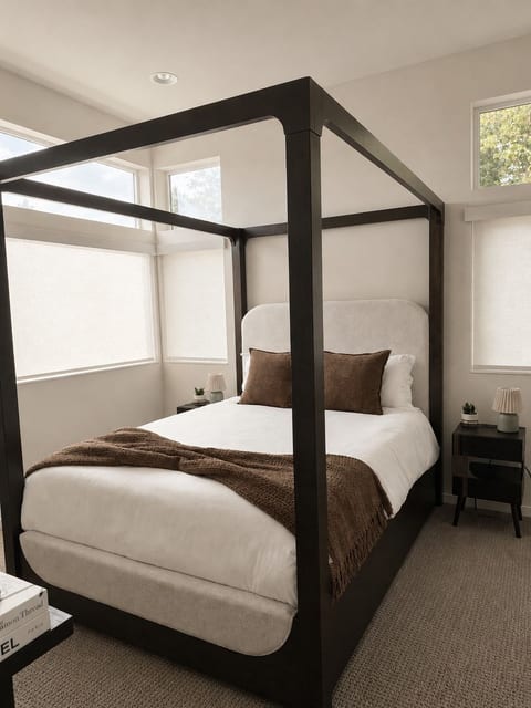 Relax in this cozy designer bedroom featuring a modern canopy bed, soft natural light, and motorized blinds easily adjusted using the attached wand.
