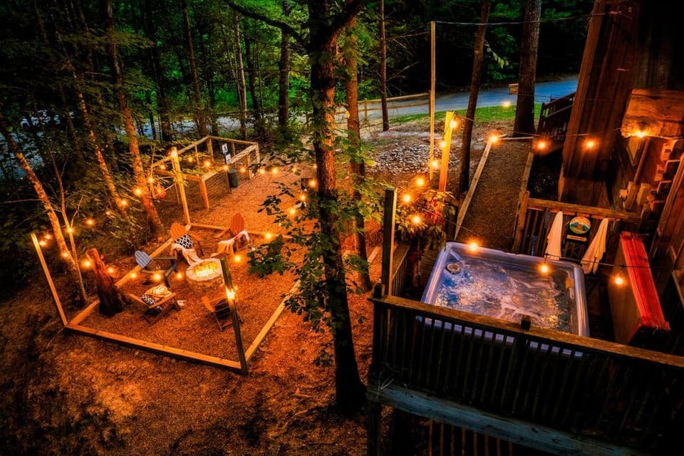 Stunning aerial view of Cubby Bear Den at night featuring private hot tub, wraparound deck, and string lights nestled in the Smoky Mountains
