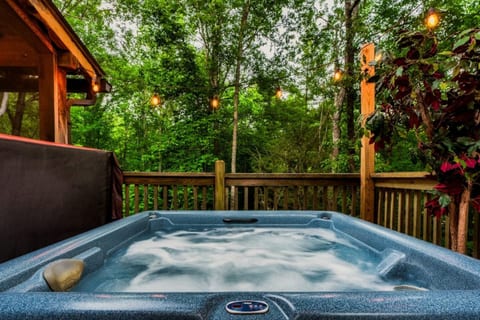 Relax in the private outdoor hot tub surrounded by lush Smoky Mountain greenery and string lights on the wraparound deck