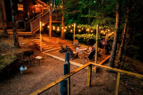Charming cabin exterior at night with glowing string lights, front porch, and steps surrounded by towering Smoky Mountain trees