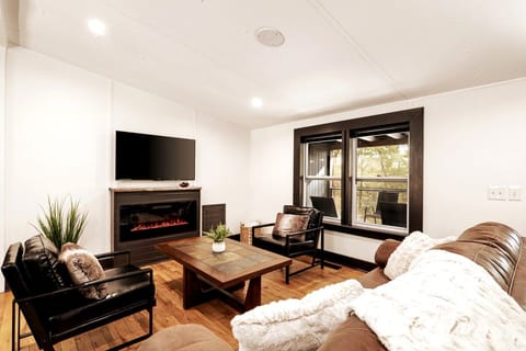 Bright and cozy living room with electric fireplace, smart TV, comfortable seating, and wooded views.