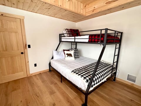This bunk room offers a Queen bed with TwinXL above. A bedside table will be added before rentals begin. Additional furniture includes a dresser, hanging rack, and luggage rack.