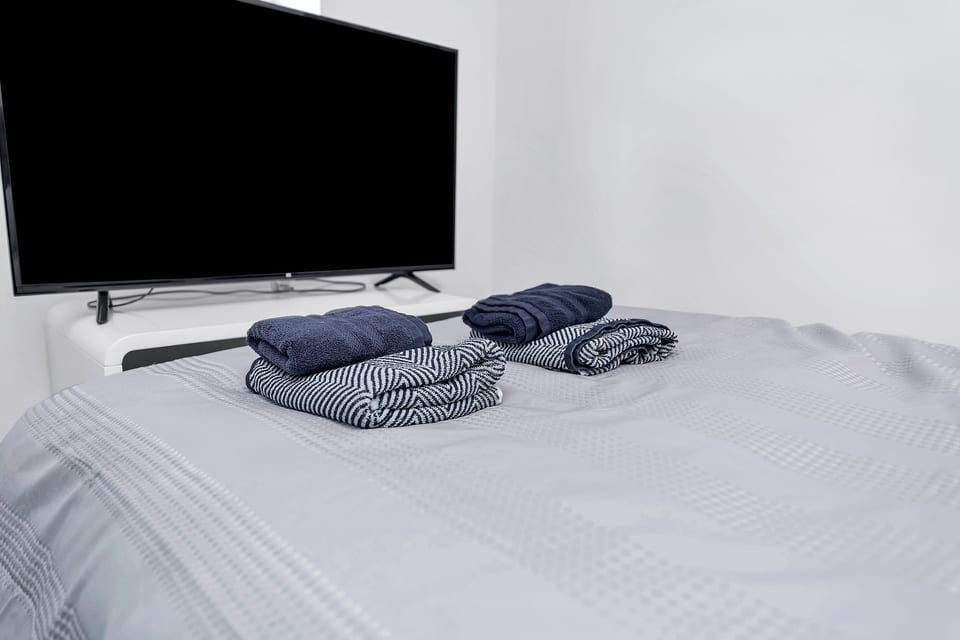 Cozy bedroom with smart TV and fresh towels—minimalist and clean.