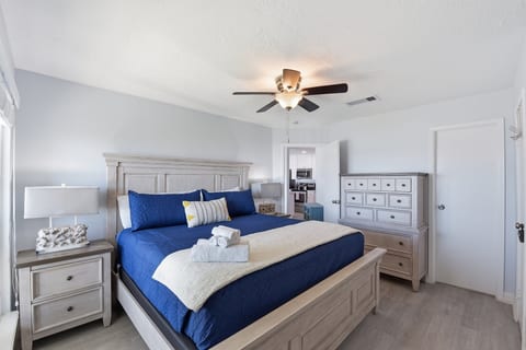 Sunny king bedroom with coastal decor, storage, and ceiling fan.