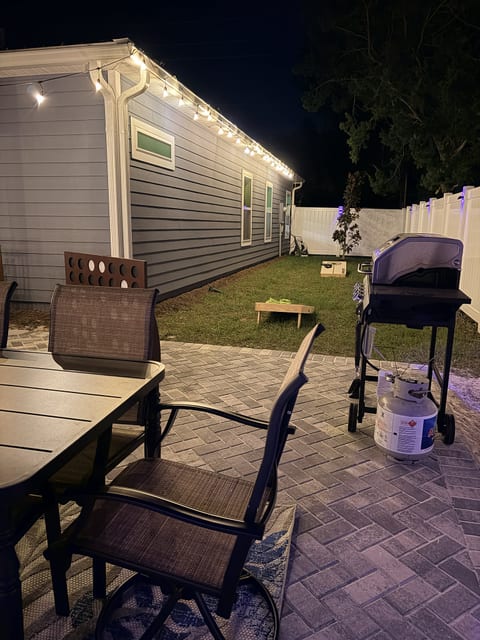 Cozy lit patio with outdoor dining, grill, and fenced backyard