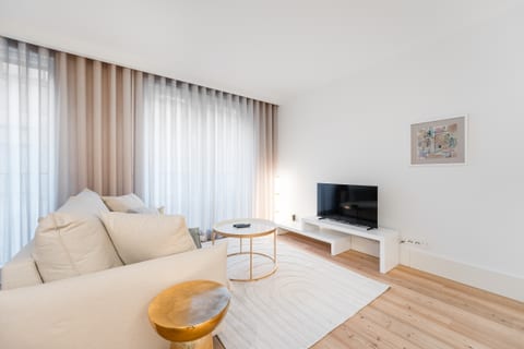 Bright minimalist lounge with cozy sofa, TV, and airy curtains