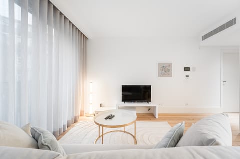 Bright minimalist lounge with sofa, TV, and floor-to-ceiling drapes