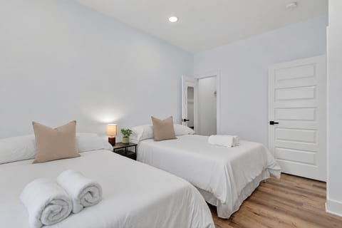 Bright double-queen room with fresh linens, hardwood floors, and soft lighting.