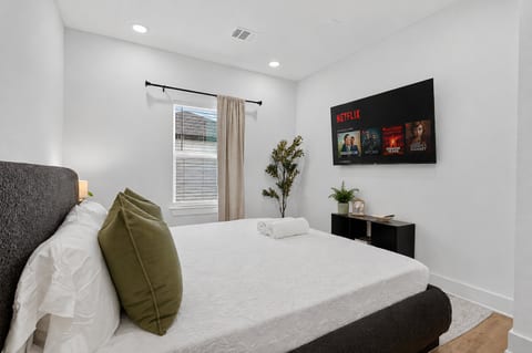 Modern, bright bedroom with smart TV & plush queen bed—relax and stream.
