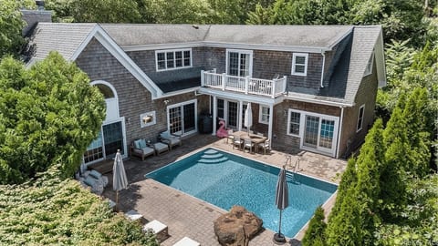 An aerial view captures the full scale of the estate, with the heated pool, wraparound patio, and primary suite balcony all visible from above.