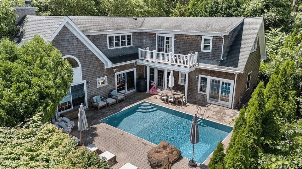 An aerial view captures the full scale of the estate, with the heated pool, wraparound patio, and primary suite balcony all visible from above.