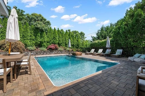 A private, tree-lined setting gives this backyard a secluded resort feel, with four chaise lounges, umbrellas, and a BBQ grill for effortless summer days.