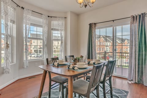 A bright and cozy dining area with large windows, stylish curtains, and a modern wooden table set for a happy meal.