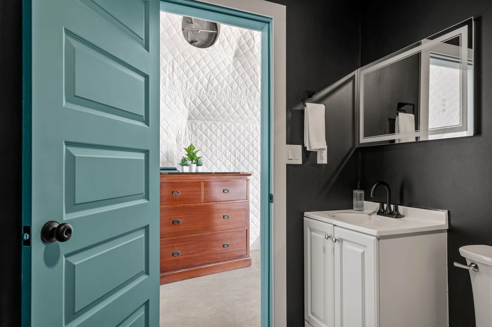 Modern bath with bold black walls, teal door, and stylish designer touches